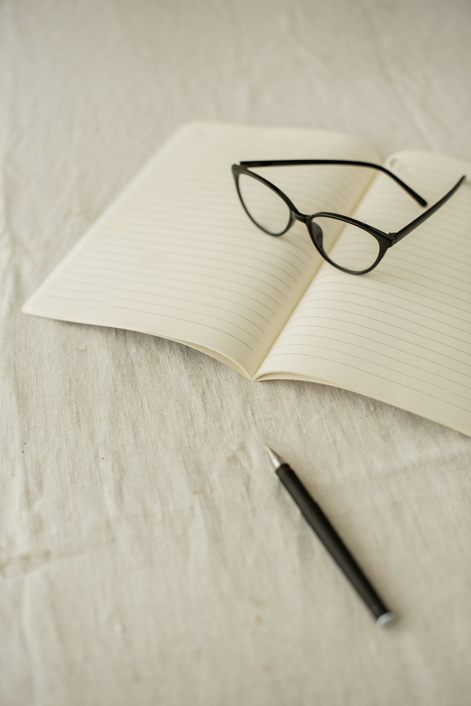 Notitieboek met leesbril en pen op een stoffen ondergrond.