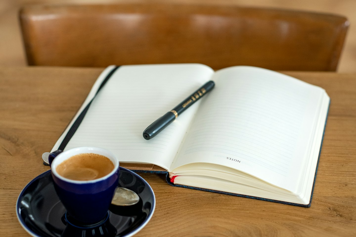 Een open notitieboekje en een kopje espresso staan op een houten tafel.